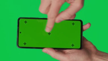 Yeşil arka planda izole edilmiş dikey yeşil renkli anahtar ekranlı akıllı telefonu tutan bir erkek. Cep telefonu bir elde. Farklı işaretler ve parmaklarla yapılan jestler. 4K dikey video şablonu