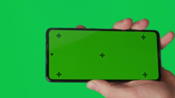 緑色の背景に隔離された垂直緑色のクロマのキー スクリーンが付いているスマートフォンを握る男性手 携帯電話を手に 指で異なる兆候とジェスチャー 4K垂直ビデオテンプレート — ストック動画