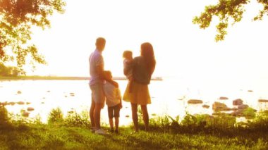 Deniz kenarında mutlu bir aile. Kırsal kesimde tarla ve ağaçlar. Gün batımının ya da güneşin sıcacık renkleri. Sevgi dolu ebeveynler ve güzel çocuklar. Aşk ve ebeveynlik kavramı.