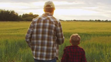 Farmer and his son in front of a sunset agricultural landscape. Man and a boy in a countryside field. The concept of fatherhood, country life, farming and country lifestyle.