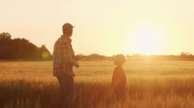 Çiftçi ve oğlu günbatımı tarımının önünde. Kırsalda bir adam ve bir çocuk. Babalık kavramı, köy hayatı, tarım ve kırsal yaşam tarzı..