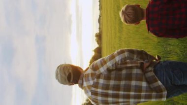 Çiftçi ve oğlu günbatımı tarımının önünde. Kırsalda bir adam ve bir çocuk. Babalık kavramı, köy hayatı, tarım ve kırsal yaşam tarzı..