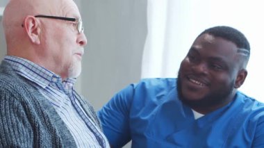 Afro-Amerikalı bakıcı ve yaşlı adam. Bakımevindeki profesyonel hemşire ve hastası. Yardım, rehabilitasyon ve sağlık hizmetleri kavramı.