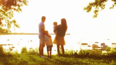 Deniz kenarında mutlu bir aile. Kırsal kesimde tarla ve ağaçlar. Gün batımının ya da güneşin sıcacık renkleri. Sevgi dolu ebeveynler ve güzel çocuklar. Aşk ve ebeveynlik kavramı.