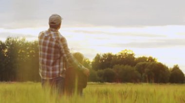 Farmer and his son in front of a sunset agricultural landscape. Man and a boy in a countryside field. The concept of fatherhood, country life, farming and country lifestyle.