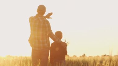 Farmer and his son in front of a sunset agricultural landscape. Man and a boy in a countryside field. The concept of fatherhood, country life, farming and country lifestyle.