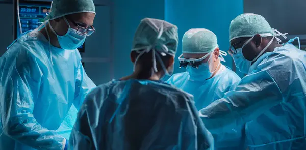 医療従事者の多様なチームは ハイテク機器と技術を使用して現代の手術室で外科手術を行います 外科医は病院で患者を救うために働いている ロイヤリティフリーのストック写真