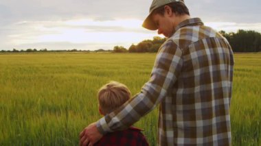 Çiftçi ve oğlu gün batımında tarım arazisine bakıyorlar. Kırsalda bir adam ve bir çocuk. Babalık kavramı, köy hayatı, tarım ve kırsal yaşam tarzı..