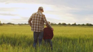 Farmer and his son in front of a sunset agricultural landscape. Man and a boy in a countryside field. The concept of fatherhood, country life, farming and country lifestyle.