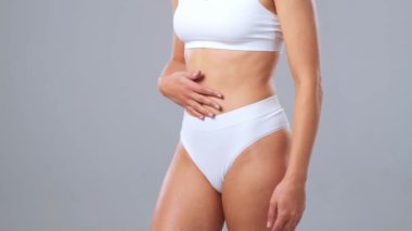 Gri arkaplanda poz veren beyaz mayo giymiş genç, fit ve güzel bir kadın. Sağlık, diyet, spor ve spor kavramı.