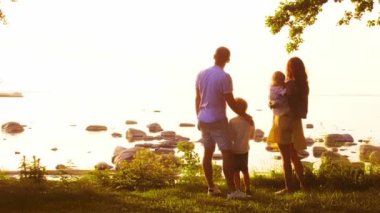 Deniz kenarında mutlu bir aile. Kırsal kesimde tarla ve ağaçlar. Gün batımının ya da güneşin sıcacık renkleri. Sevgi dolu ebeveynler ve güzel çocuklar. Aşk ve ebeveynlik kavramı.
