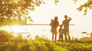 Deniz kenarında mutlu bir aile. Kırsal kesimde tarla ve ağaçlar. Gün batımının ya da güneşin sıcacık renkleri. Sevgi dolu ebeveynler ve güzel çocuklar. Aşk ve ebeveynlik kavramı.