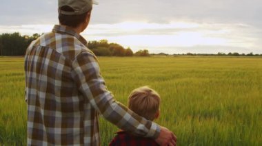 Çiftçi ve oğlu günbatımı tarımının önünde. Kırsalda bir adam ve bir çocuk. Babalık kavramı, köy hayatı, tarım ve kırsal yaşam tarzı..
