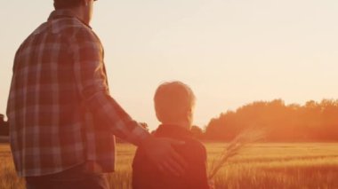 Farmer and his son in front of a sunset agricultural landscape. Man and a boy in a countryside field. The concept of fatherhood, country life, farming and country lifestyle.