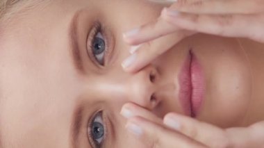 Cilt bakımı kremi süren genç, güzel ve doğal sarışın kadının stüdyo portresi. Dikey video. Yüz gerdirme, kozmetik ve makyaj konsepti.