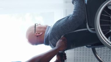 Afro-Amerikalı bakıcı ve yaşlı adam. Bakımevindeki profesyonel hemşire ve hastası. Yardım, rehabilitasyon ve sağlık hizmetleri kavramı. Dikey video.