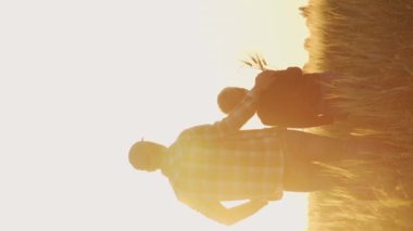 Çiftçi ve oğlu günbatımı tarımının önünde. Kırsalda bir adam ve bir çocuk. Babalık kavramı, köy hayatı, çiftçilik ve kırsal yaşam tarzı. Dikey video.