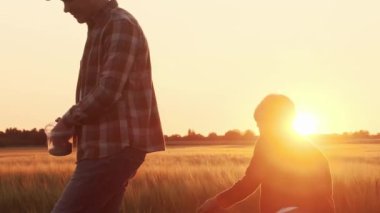 Farmer and his son in front of a sunset agricultural landscape. Man and a boy in a countryside field. The concept of fatherhood, country life, farming and country lifestyle.