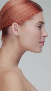 Cilt bakımı kremi süren genç, güzel ve doğal kızıl saçlı kadının stüdyo portresi. Yüz gerdirme, kozmetik ve makyaj konsepti. Dikey video.