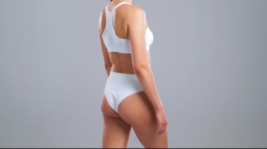 Gri arkaplanda poz veren beyaz mayo giymiş genç, fit ve güzel bir kadın. Sağlık, diyet, spor ve spor kavramı.
