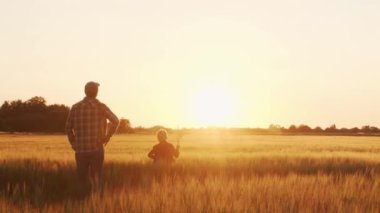 Farmer and his son in front of a sunset agricultural landscape. Man and a boy in a countryside field. The concept of fatherhood, country life, farming and country lifestyle.