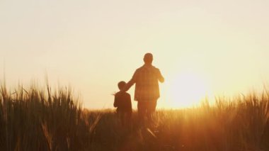 Farmer and his son in front of a sunset agricultural landscape. Man and a boy in a countryside field. The concept of fatherhood, country life, farming and country lifestyle.
