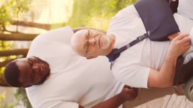 Afro-Amerikalı bakıcı ve yaşlı adam. Bakımevindeki profesyonel hemşire ve hastası. Yardım, rehabilitasyon ve sağlık hizmetleri kavramı. Dikey video.