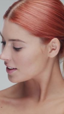 Cilt bakımı kremi süren genç, güzel ve doğal kızıl saçlı kadının stüdyo portresi. Yüz gerdirme, kozmetik ve makyaj konsepti. Dikey video.