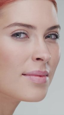 Gülümseyen genç, güzel ve doğal kızıl saçlı kadının stüdyo portresi. Yüz gerdirme, kozmetik ve makyaj konsepti. Dikey video.
