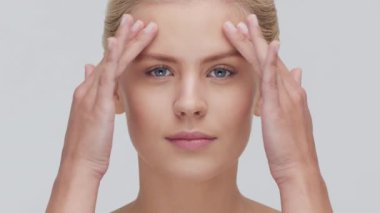 Yüzüne nazikçe masaj yapan genç, güzel ve doğal sarışın kadının stüdyo portresi. Yüz gerdirme, kozmetik ve makyaj konsepti.