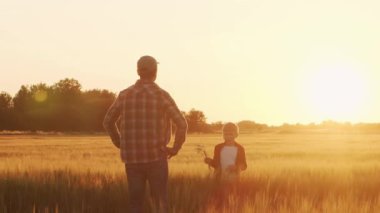 Farmer and his son in front of a sunset agricultural landscape. Man and a boy in a countryside field. The concept of fatherhood, country life, farming and country lifestyle.