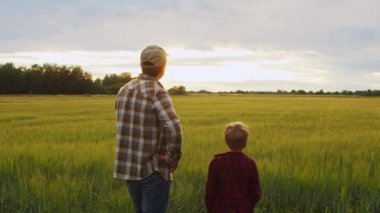 Farmer and his son in front of a sunset agricultural landscape. Man and a boy in a countryside field. The concept of fatherhood, country life, farming and country lifestyle.