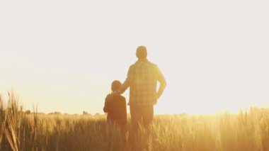 Farmer and his son in front of a sunset agricultural landscape. Man and a boy in a countryside field. The concept of fatherhood, country life, farming and country lifestyle.