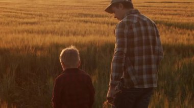 Farmer and his son in front of a sunset agricultural landscape. Man and a boy in a countryside field. The concept of fatherhood, country life, farming and country lifestyle.
