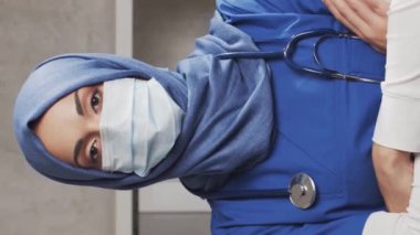 Dikey video. Hastane ofisinde çalışan profesyonel tıp doktoru koruyucu maskeli genç ve çekici bir kadın doktorun portresi. Tıbbi konsept.