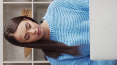 Genç ve çekici bir kadın evde dizüstü bilgisayar kullanarak çalışıyor. Serbest çalışan ya da öğrenci çevrimiçi konuşma yapıyor. Dikey video.