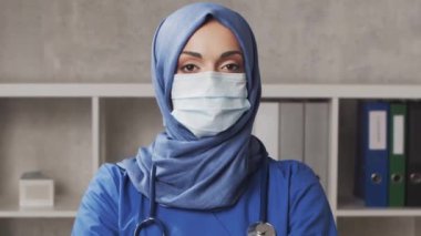 Hastane ofisinde çalışan profesyonel tıp doktoru koruyucu maskeli genç ve çekici bir kadın doktorun portresi. Tıbbi video konsepti.