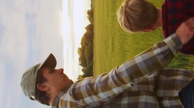 Çiftçi ve oğlu günbatımı tarımının önünde. Kırsalda bir adam ve bir çocuk. Babalık kavramı, köy hayatı, çiftçilik ve kırsal yaşam tarzı. Dikey video.