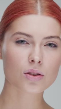 Cilt bakımı kremi süren genç, güzel ve doğal kızıl saçlı kadının stüdyo portresi. Yüz gerdirme, kozmetik ve makyaj konsepti. Dikey video.