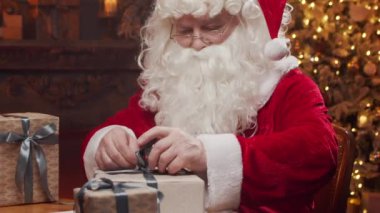 Santa Clauss atölyesi. Noel Baba masanın arkasında şömine ve Noel ağacı olan hediyesini paketlemekle meşgul. Klasik bir Noel sahnesi..