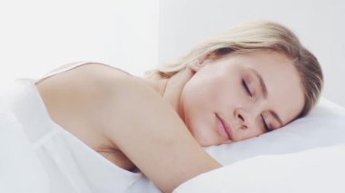 Huzurlu, huzurlu bir sahne. Genç bir kadın, rahat bir şekilde yatakta uyuyor. Yumuşak, doğal ışıklandırmayla. Rahatlama, dinlenme ve sükunet temaları için mükemmel. Ev kavramı.