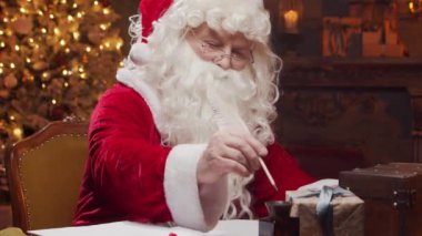 Santa Clauss atölyesi. Noel Baba masanın arkasında şömine ve Noel ağacı olan hediyesini paketlemekle meşgul. Klasik bir Noel sahnesi..