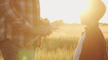 Farmer and his son in front of a sunset agricultural landscape. Man and a boy in a countryside field. The concept of fatherhood, country life, farming and country lifestyle.