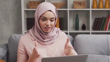 Türbanlı ve koruyucu maskeli genç Müslüman kızın yakın plan portresi. Üzgün Orta Doğulu kadın evde kameranın önünde oturuyor. Yakın plan..