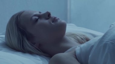 Genç bir kadın geceleri yatakta uzanıyor ve uykusuzluk hastalığına yakalanıyor. Güzel sarışın, uyuyan kız. Yatak odasında alacakaranlık, pencereden ay ışığı. Uykusuzluk, sağlık ve dinlenme konsepti. Ev