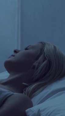 Genç bir kadın geceleri yatakta uzanıyor ve uykusuzluk hastalığına yakalanıyor. Güzel sarışın, uyuyan kız. Yatak odasında alacakaranlık, pencereden ay ışığı. Uykusuzluk, sağlık ve dinlenme konsepti. Dikey