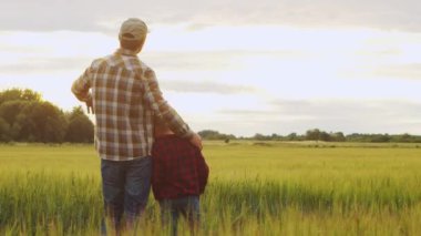 Farmer and his son in front of a sunset agricultural landscape. Man and a boy in a countryside field. The concept of fatherhood, country life, farming and country lifestyle.