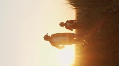 Çiftçi ve oğlu günbatımı tarımının önünde. Kırsalda bir adam ve bir çocuk. Babalık kavramı, köy hayatı, çiftçilik ve kırsal yaşam tarzı. Dikey video.