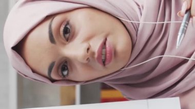 Türbanlı ve koruyucu maskeli genç Müslüman kızın yakın plan portresi. Üzgün Orta Doğulu kadın evde kameranın önünde oturuyor..