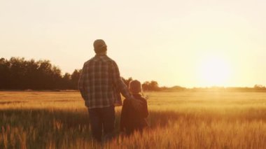 Farmer and his son in front of a sunset agricultural landscape. Man and a boy in a countryside field. The concept of fatherhood, country life, farming and country lifestyle.